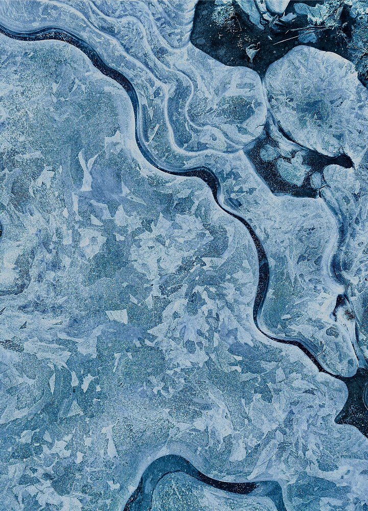 Wavy abstract ice pattern with curved dark creases and light blue crystalline textures creating a mosaic of swirling shapes across the surface.