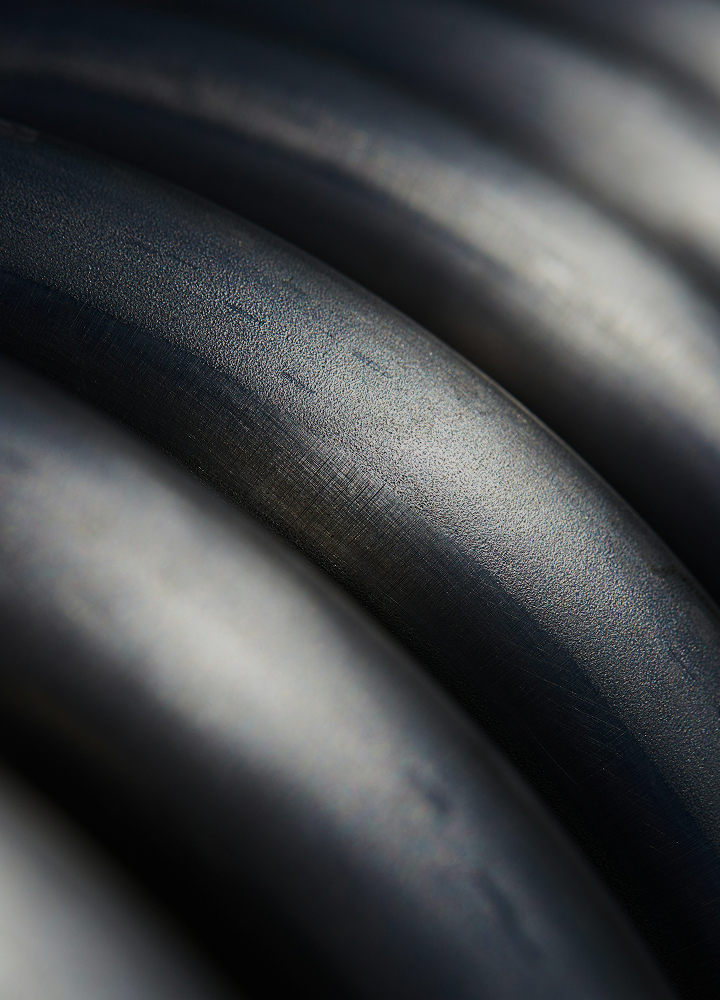 Close-up of dark textured curved surfaces forming layered, smooth arcs with subtle highlights and shallow depth in a monochrome palette.