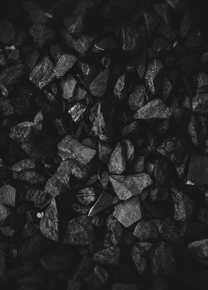 a close-up view of rough, jagged black rocks or gravel densely packed together with varying light and shadow across the uneven surfaces