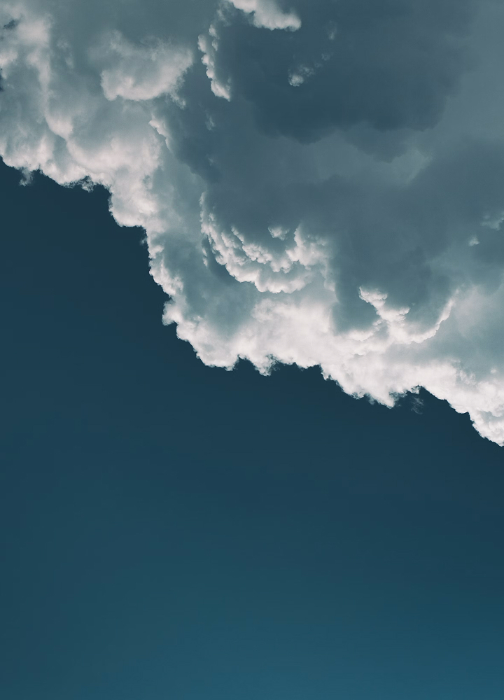 Cloudy sky with a large, white, billowing cloud formation occupying the upper portion and a clear deep blue backdrop below.