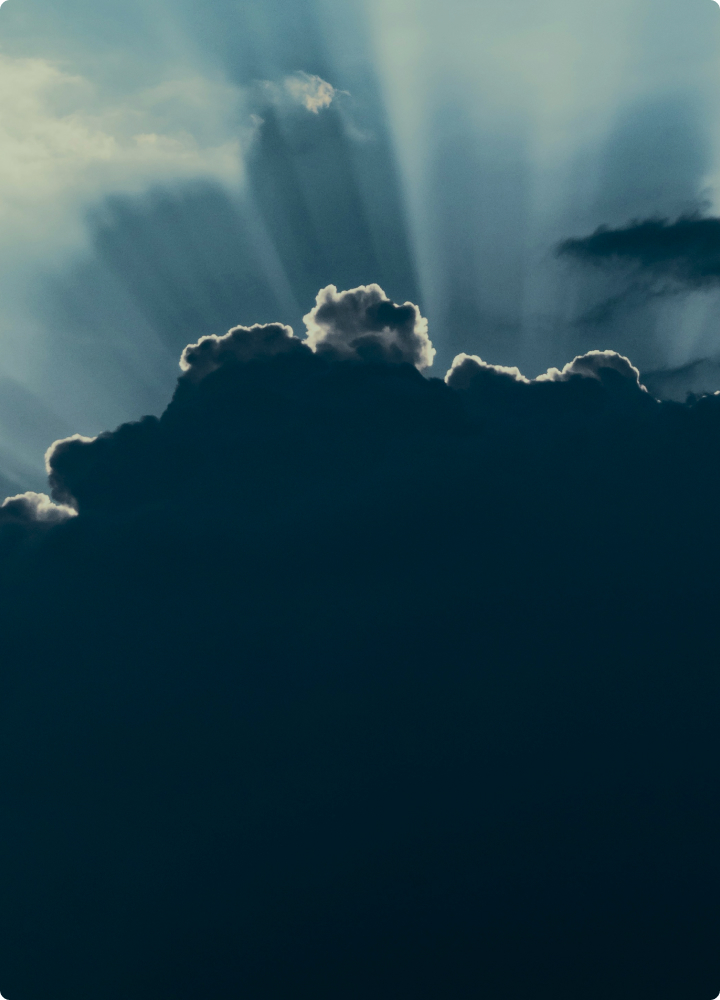 Sunlit clouds with dramatic crepuscular rays streaming upward through the sky, casting a bright glow around the cloud edges against a deep blue backdrop.