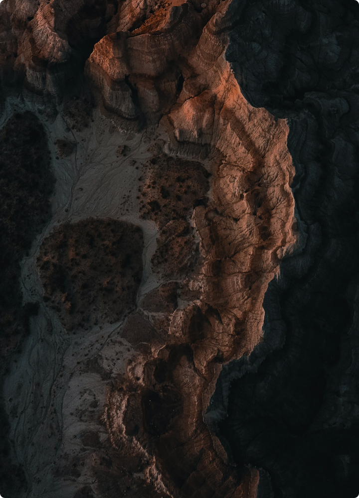 Rugged canyon walls bathed in warm, reddish light with dark shadowed crevices and rocky textures along a narrow cliffside formation.