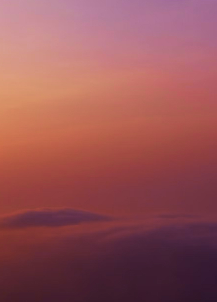 Soft pastel sunset sky with gradient tones of peach, pink, and purple, faint distant horizon near the bottom with wispy clouds.