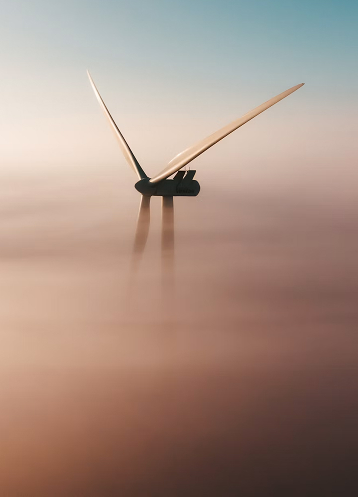 Wind turbine standing in a hazy, pastel-colored landscape with two blades visible above a soft, gradient mist.