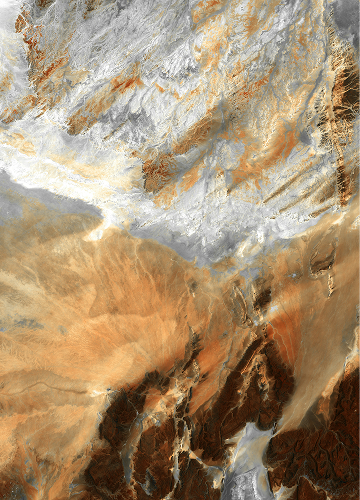 Colorful, abstract aerial terrain with layered browns, oranges, and whites; rugged, diagonal patterns suggesting desert canyons and eroded rock formations.