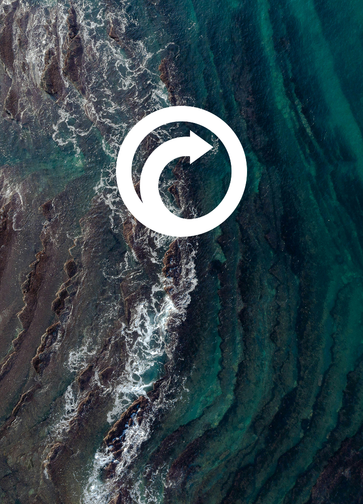 Aerial view of turquoise ocean with rocky shorelines and white waves, overlaid by a white circular refresh icon in the center.