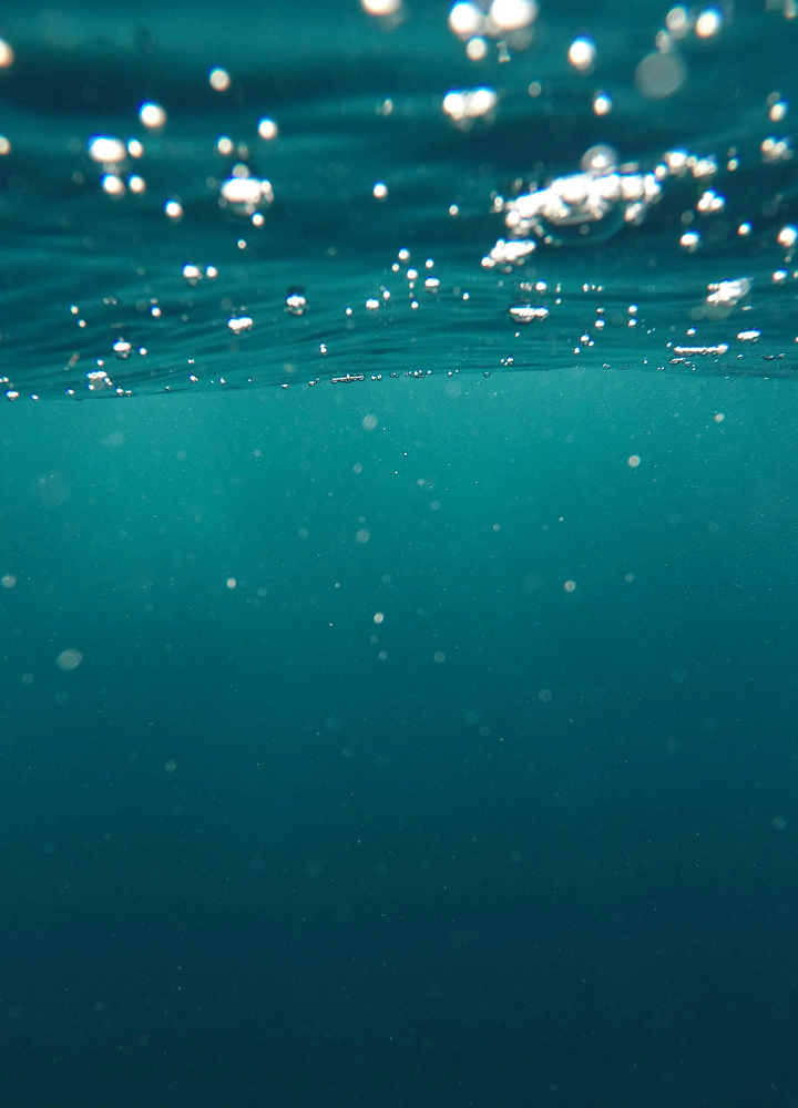 Underwater scene with turquoise water, air bubbles rising toward the surface, and a hazy, dotted depth below.