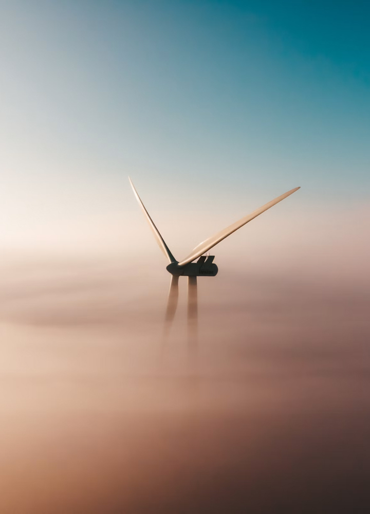 Wind turbine emerging from soft pastel clouds at sunrise or sunset, with long slender blades and a tranquil gradient sky from teal to peach.