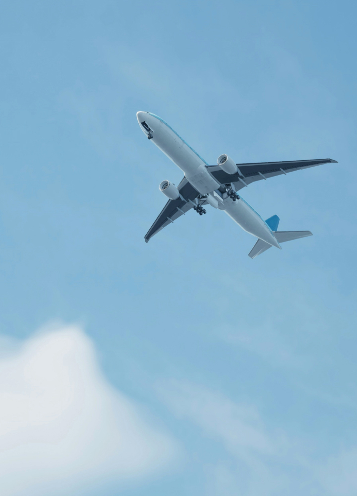 Passenger jet flying overhead, underside view against blue sky with extended landing gear and two engines under wings, white fuselage, blue tail fin visible.
