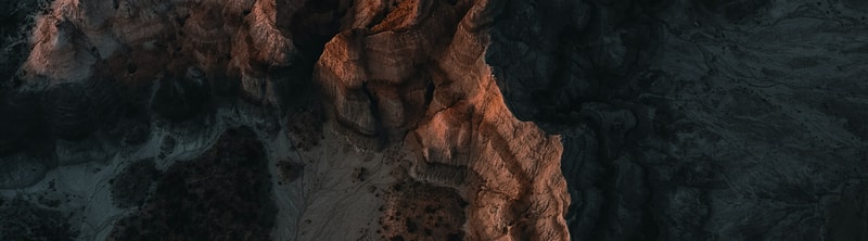 Aerial view of a rocky canyon with warm orange sunlit walls on the left center, transitioning to dark shaded rock on the right and bottom.
