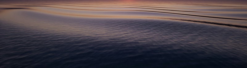 Serene sea at sunset with gentle ripples reflecting warm pink and orange hues across the calm water.