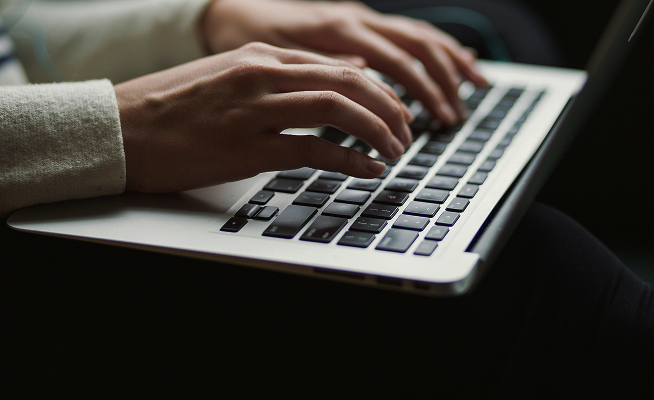 Hands typing on a slim laptop keyboard, fingers resting on dark keys, close-up shot with a soft, focused feel and a light sleeve visible.