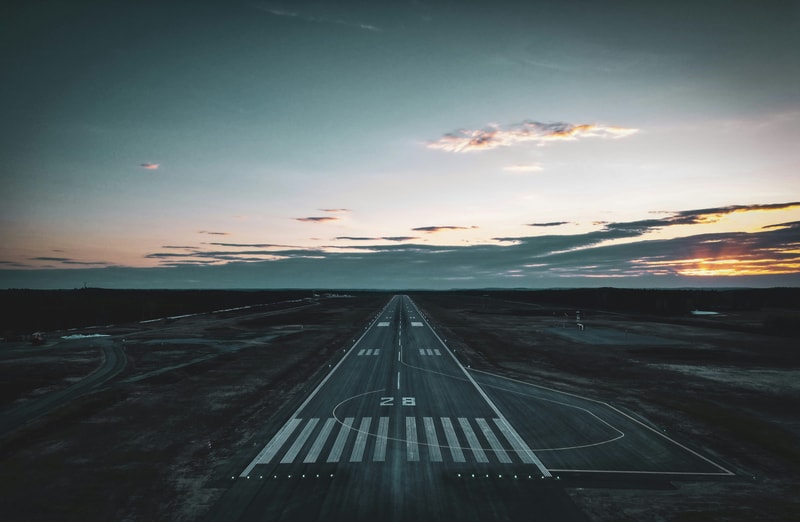 An empty runway extending into the horizon at dusk, with a long, straight taxiway, runway markings, and a dramatic sky of blue and orange clouds.