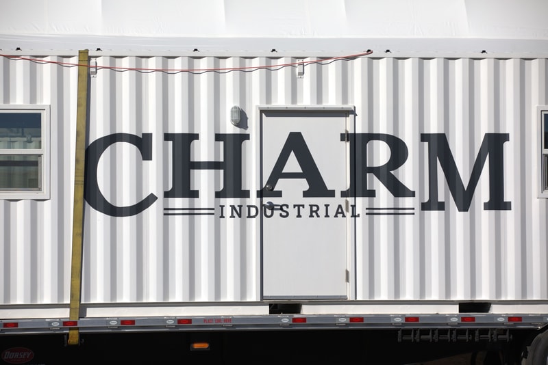 large white industrial shipping container trailer with bold "CHARM" letters and "INDUSTRIAL" text overlay, door in center, small window on left, wired lighting above.