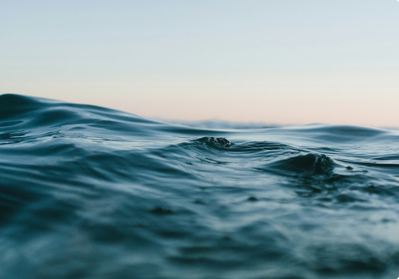 Smooth ocean surface with small waves, turquoise-blue water, soft horizon, and a pale gradient sky in the distance.