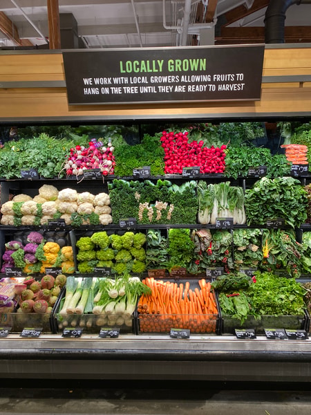 Fresh produce display in a grocery store with a variety of leafy greens, root vegetables, and bright orange carrots arranged in organized shelves.