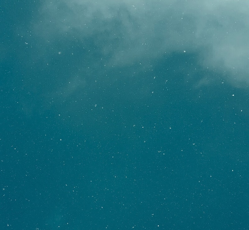 A teal underwater scene with small white particles drifting, light mist toward the upper area, creating a calm, grainy oceanic appearance.